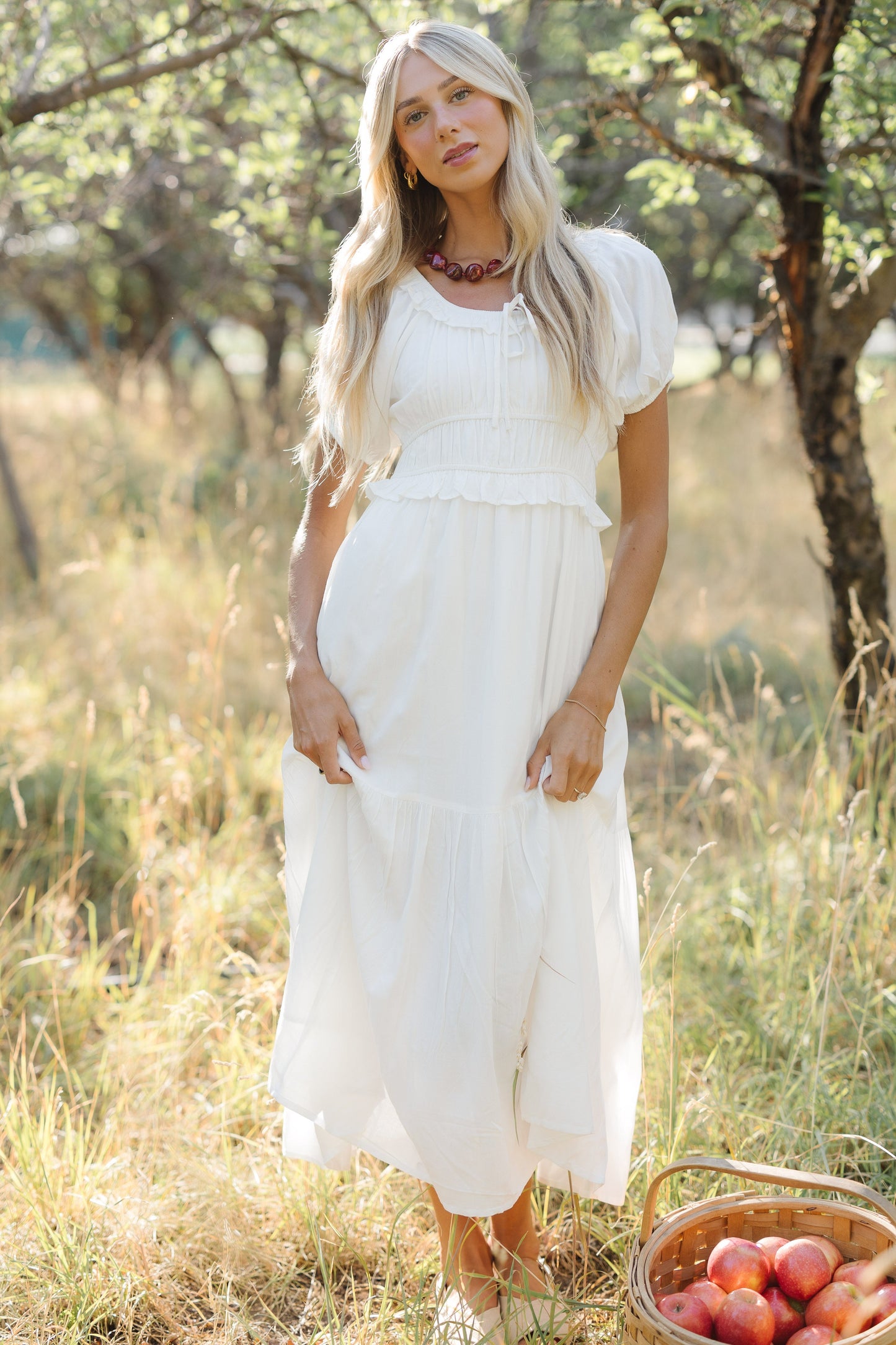 Young woman wearing a modest white midi dress with a ruffled scoop neckline, puff sleeves, wide waistband and full ruffled skirt.