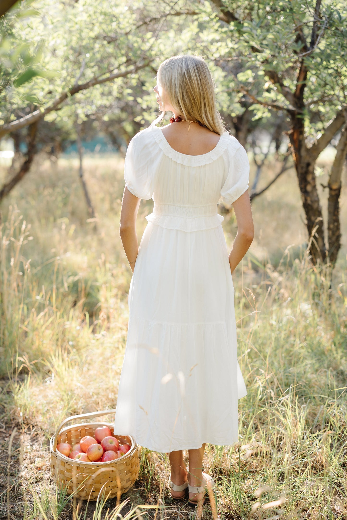 Back view of a woman wearing a white midi dress with a scoop necklien, puff sleeves and wide bottom ruffle.