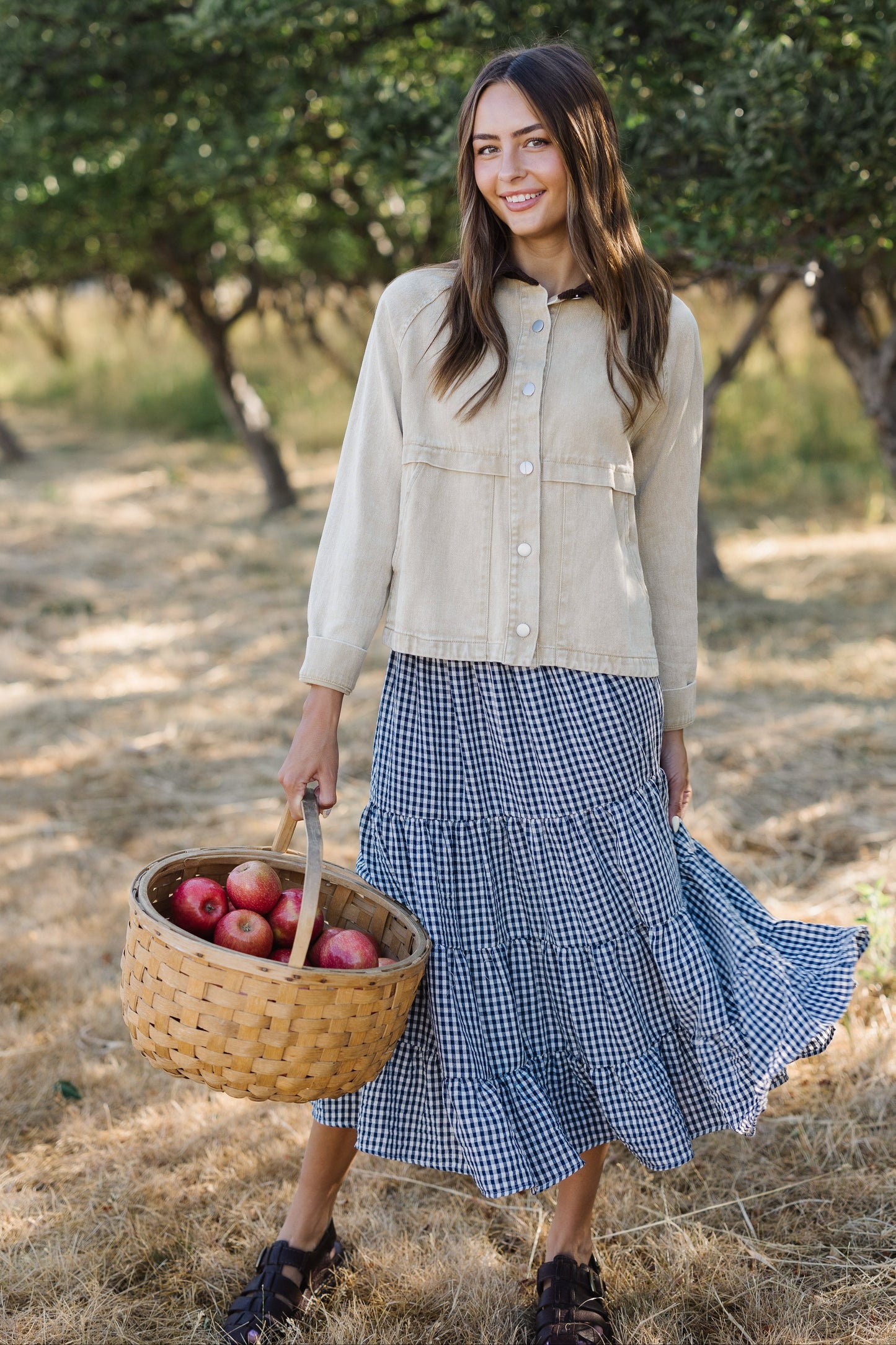 Young woman wearing a modest light beige woven jacket with metal buttons and decorative seam details.