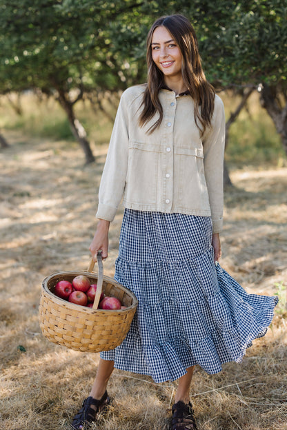 Young woman wearing a modest light beige woven jacket with metal buttons and decorative seam details.
