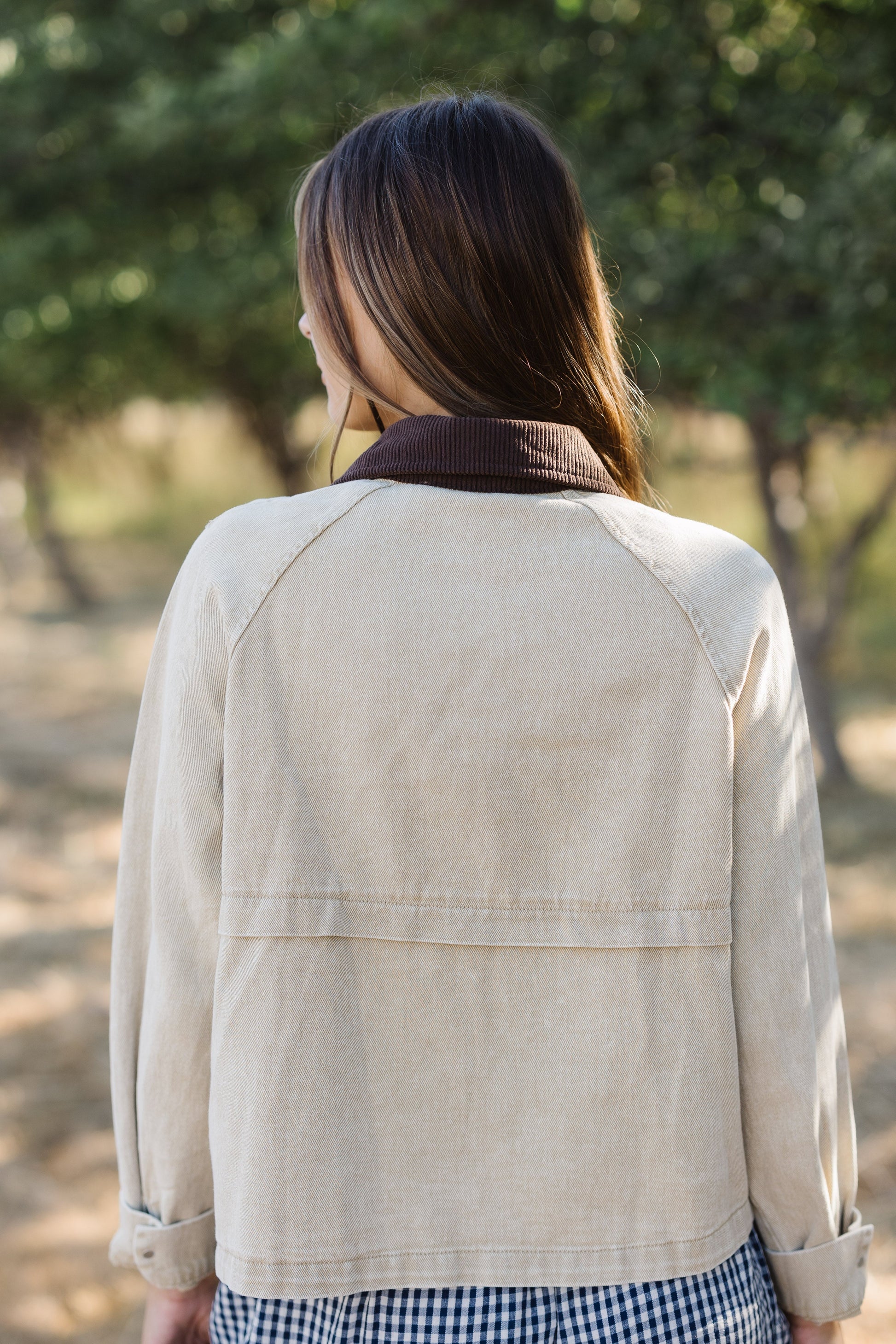 Back view of a woman wearing a tan loose fitting jacket with a brown corduroy collar and long sleeves.