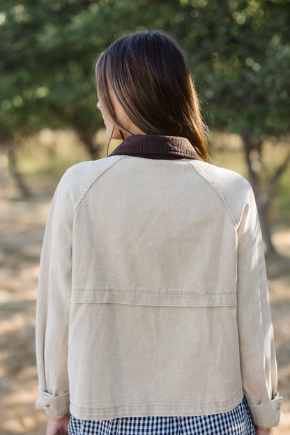 Back view of a woman wearing a tan loose fitting jacket with a brown corduroy collar and long sleeves.