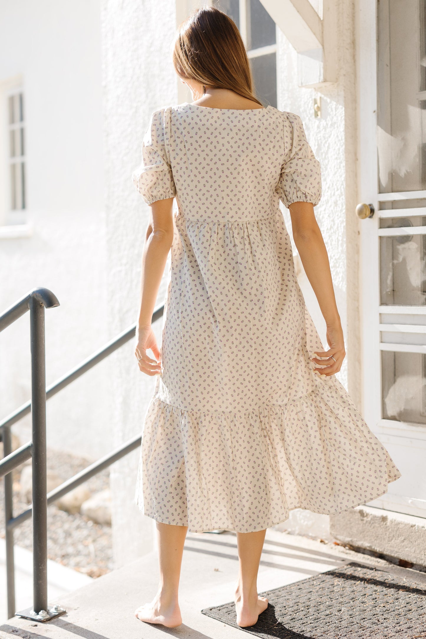 Back view of a woman wearing a cream print dress with a wide bottome ruffle and large puff sleeves.