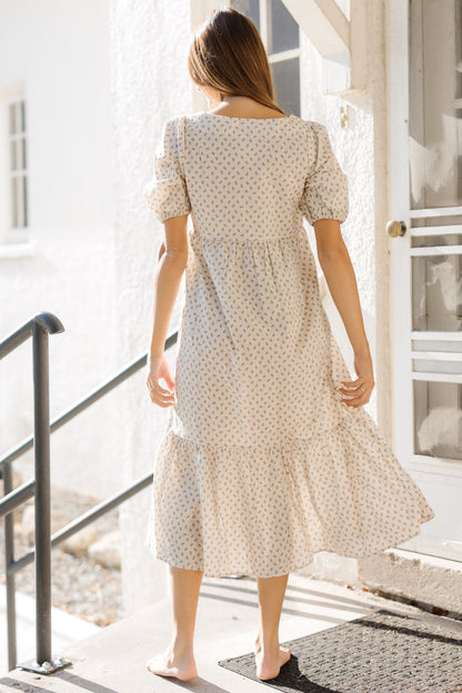 Back view of a woman wearing a cream print dress with a wide bottome ruffle and large puff sleeves.