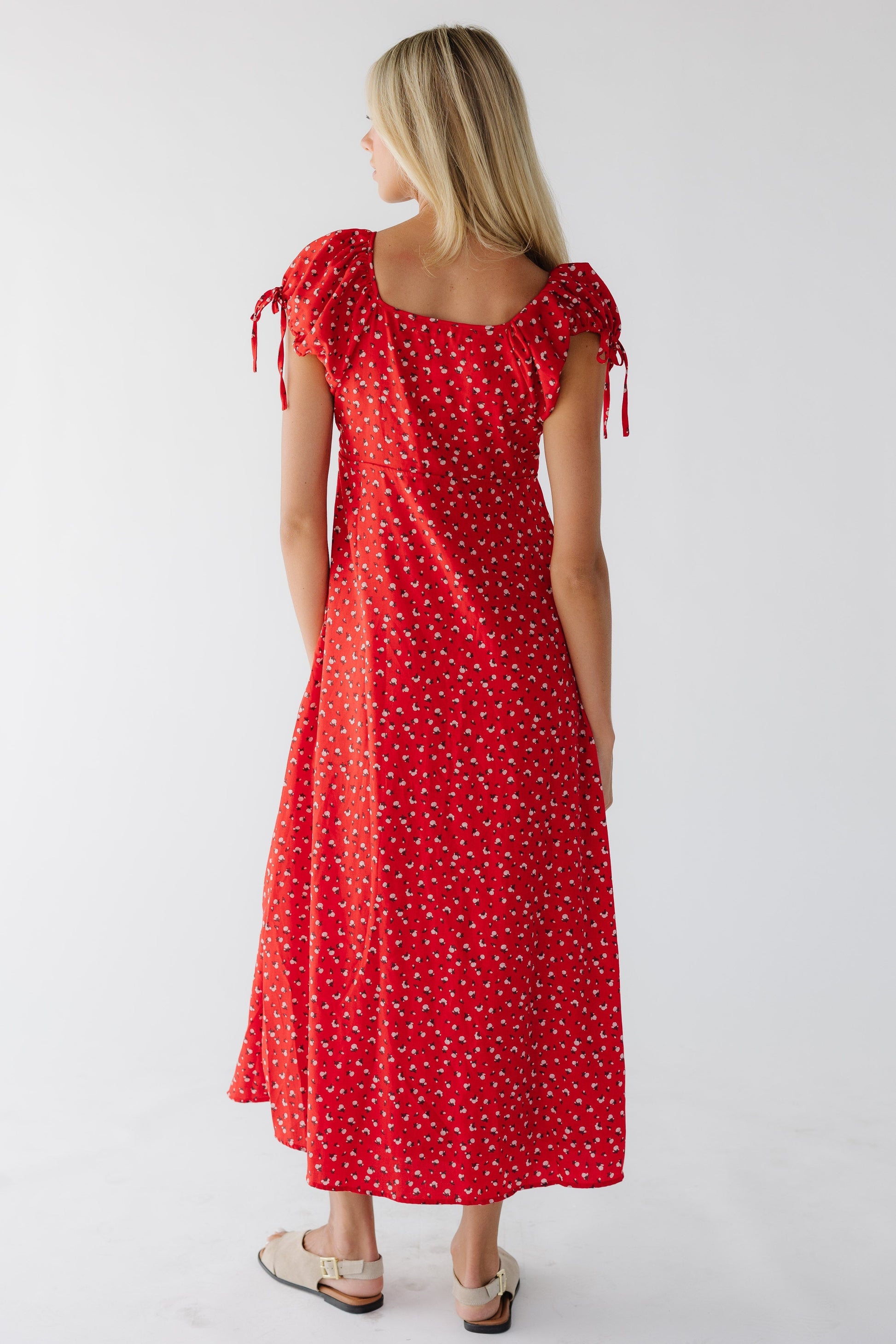 Back view of a woman wearing a red floral A-line dess with a square back neckline and puff sleeves.