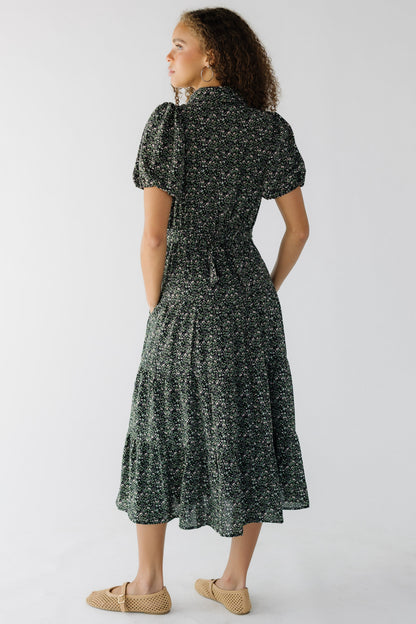 Back view of a teenage girl weaing a black floral, tiered midi dress wtih short sleve and a clser fitting waist.