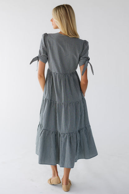 Back view of a woman wearing a navy & white gingham midi tiered dress with short puff sleeves.
