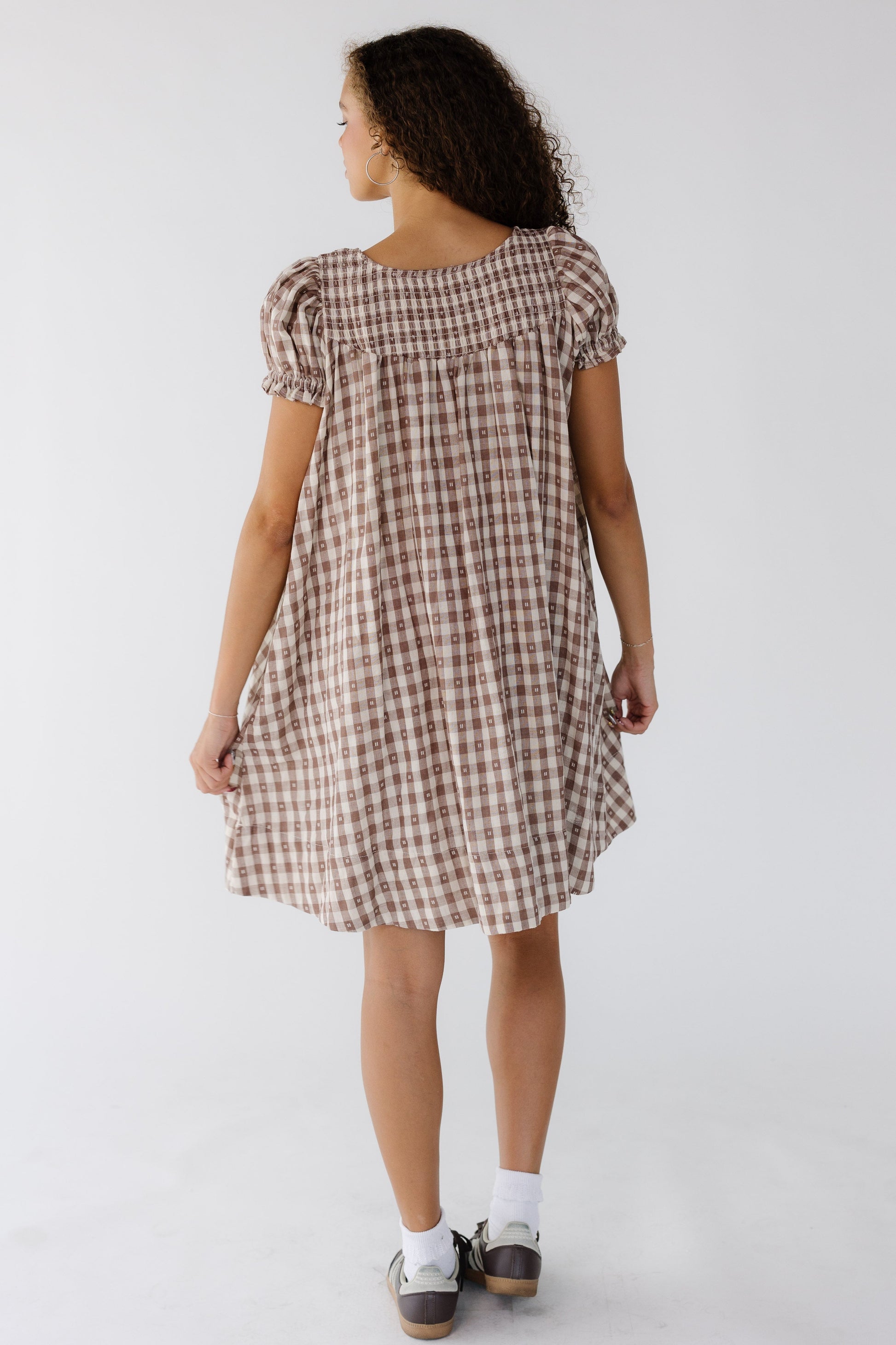 Back view of a woman a brown & white gingham dress with short puff sleeves and a back smocked yoke.
