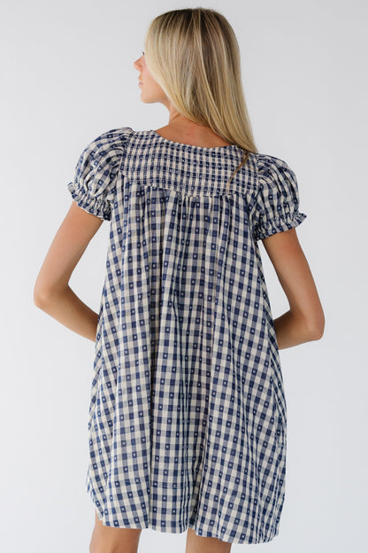 Back view of a woman wearing a navy & whie gingham knee dress with short puff sleeves and a smocked back neckline.