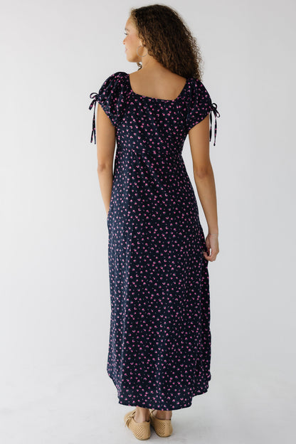 Back view of a woman wearing a navy & pink floral midi-maxi dress with a square neckline and short puff sleeves.