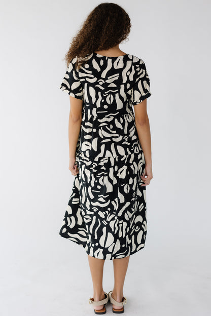 Back view of a teenge girl wearing a loose fitting black & cream midi dress with short sleeves.