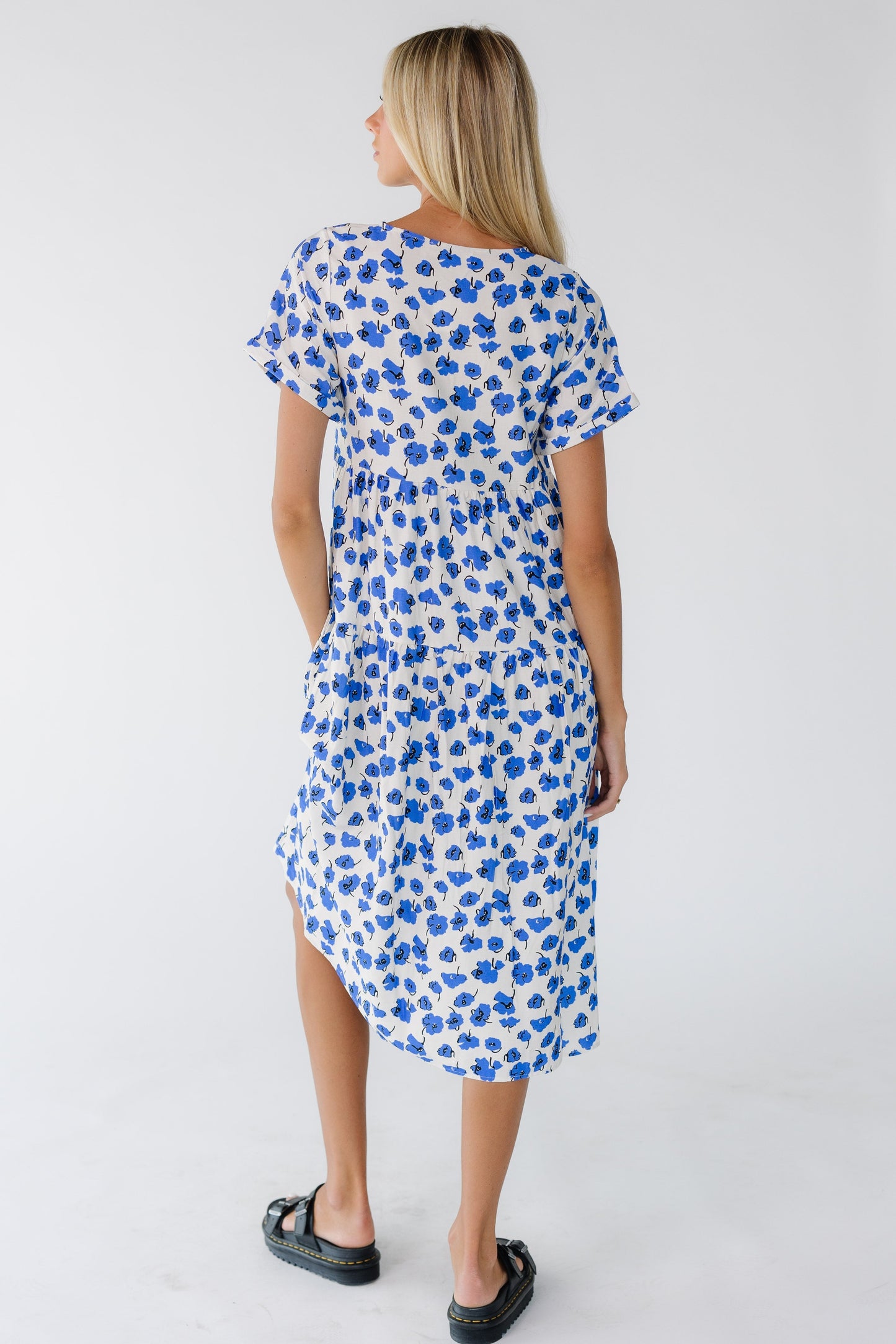 Back view of a woman wearing a blue & white floral midi dress with short sleeves.