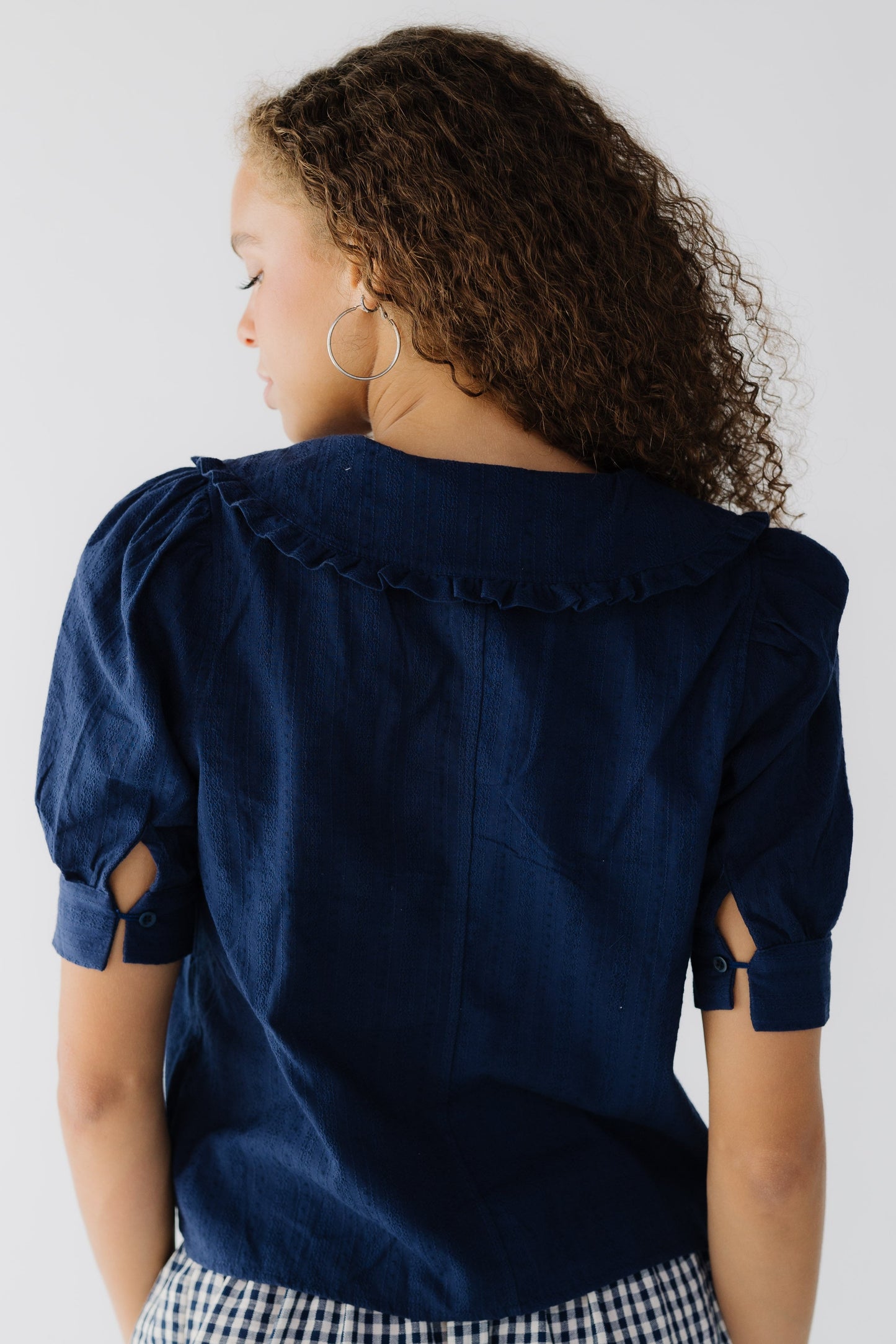 Back view of a teenage girlwearing a navy blouse with short puff sleeves and a ruffle edged collar.