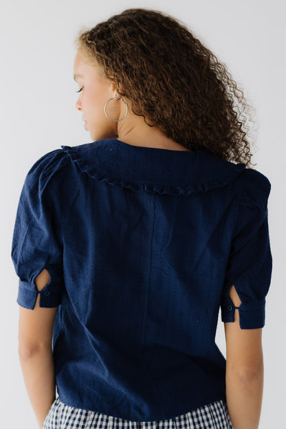 Back view of a teenage girlwearing a navy blouse with short puff sleeves and a ruffle edged collar.