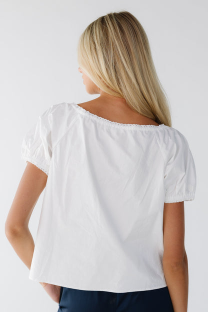 Back view of a woman wearing a white loose fitting blouse with short puff sleeves.