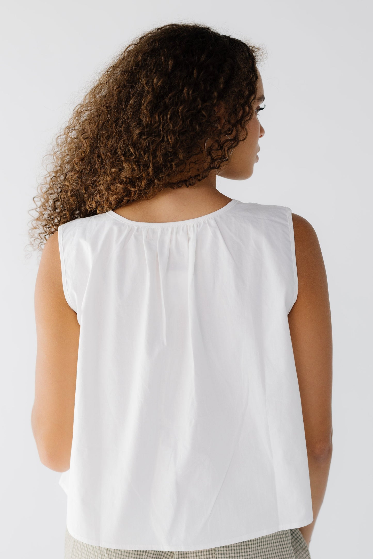 Back view of a woman wearing a white sleeveless loose fitting blouse.