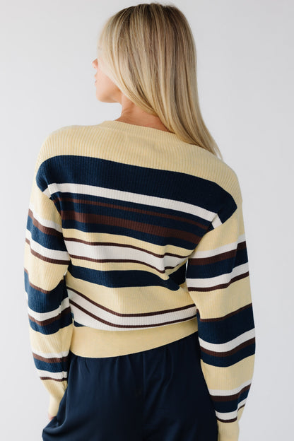 Back view of a young woman wearing a yellow and multi-color stripe sweater with long sleeves.