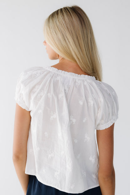Back view of a woman wearing a white embroidered blouse with a ruffled neckline and short puff sleeves.