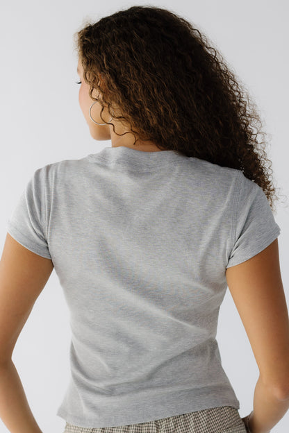 Back view of a woman wearing a close fitting grey short sleeve tee with a wide ribbed neckline.