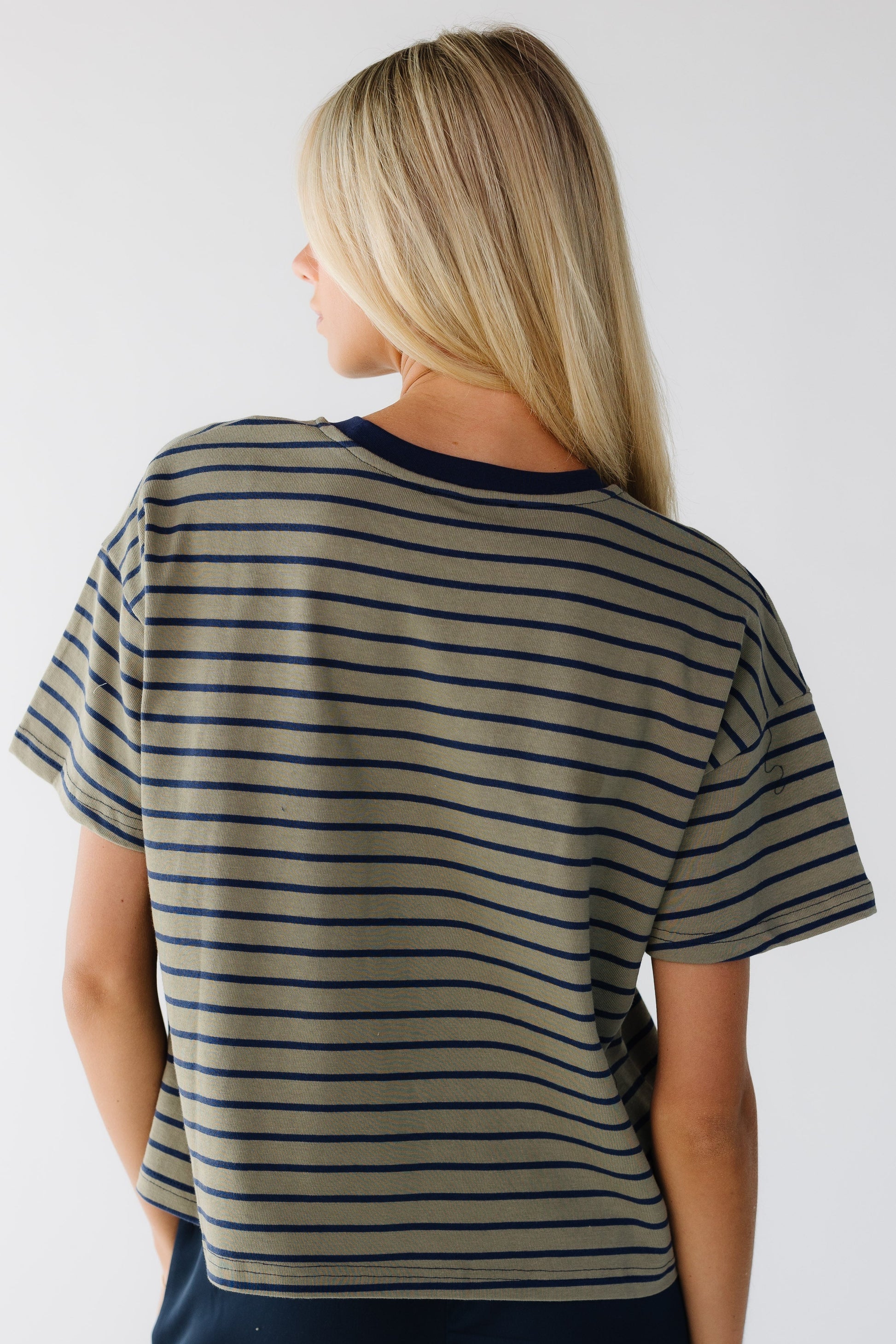 Back view of a woman weariang a olive and navy stirpe loose fitting tee with short sleeves.