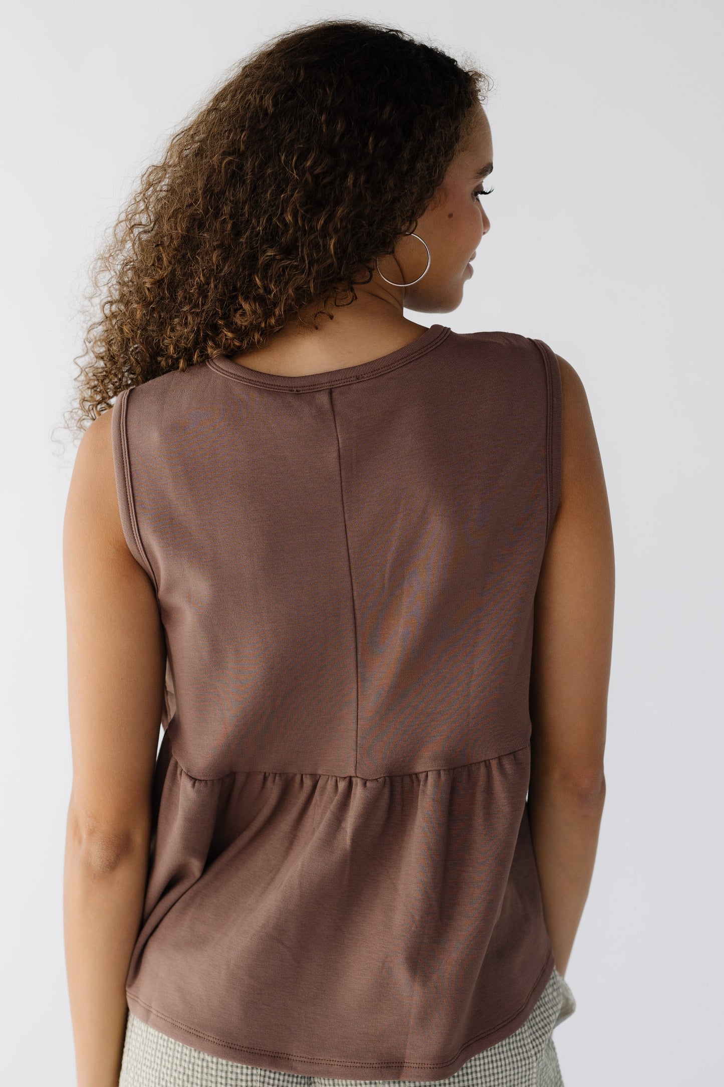 Back view of a young woman wearing a loose fitting  sleveless blouse in light brown.