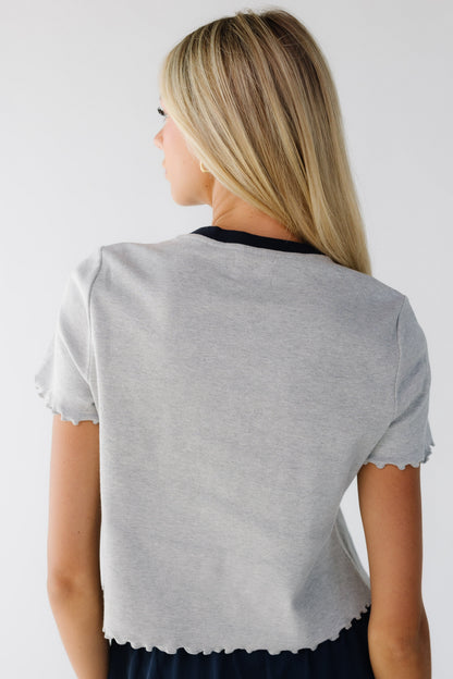 Back view of a young woman wearing a grey top with ruffled lettuce hems and a dark crew neckline.