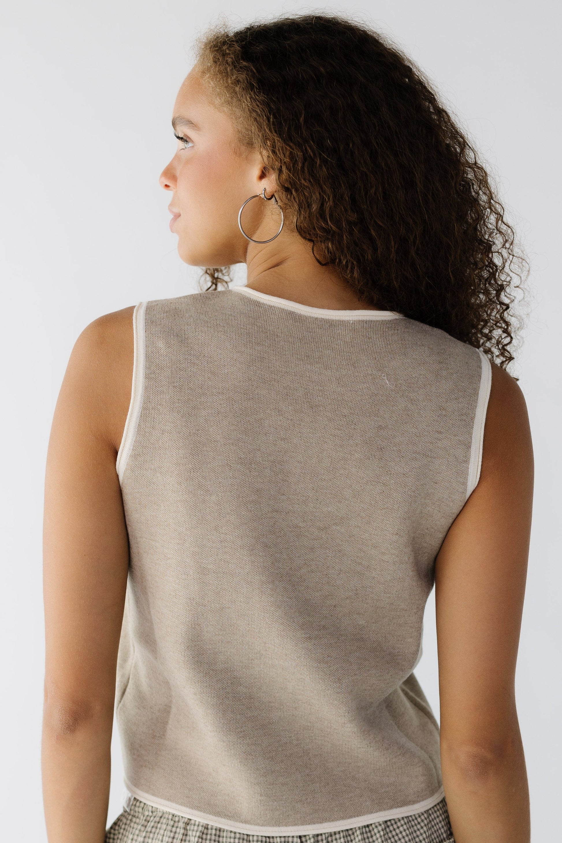 Back view of a teenage girl wearing a sleeveless beige top with cream rolled hems.