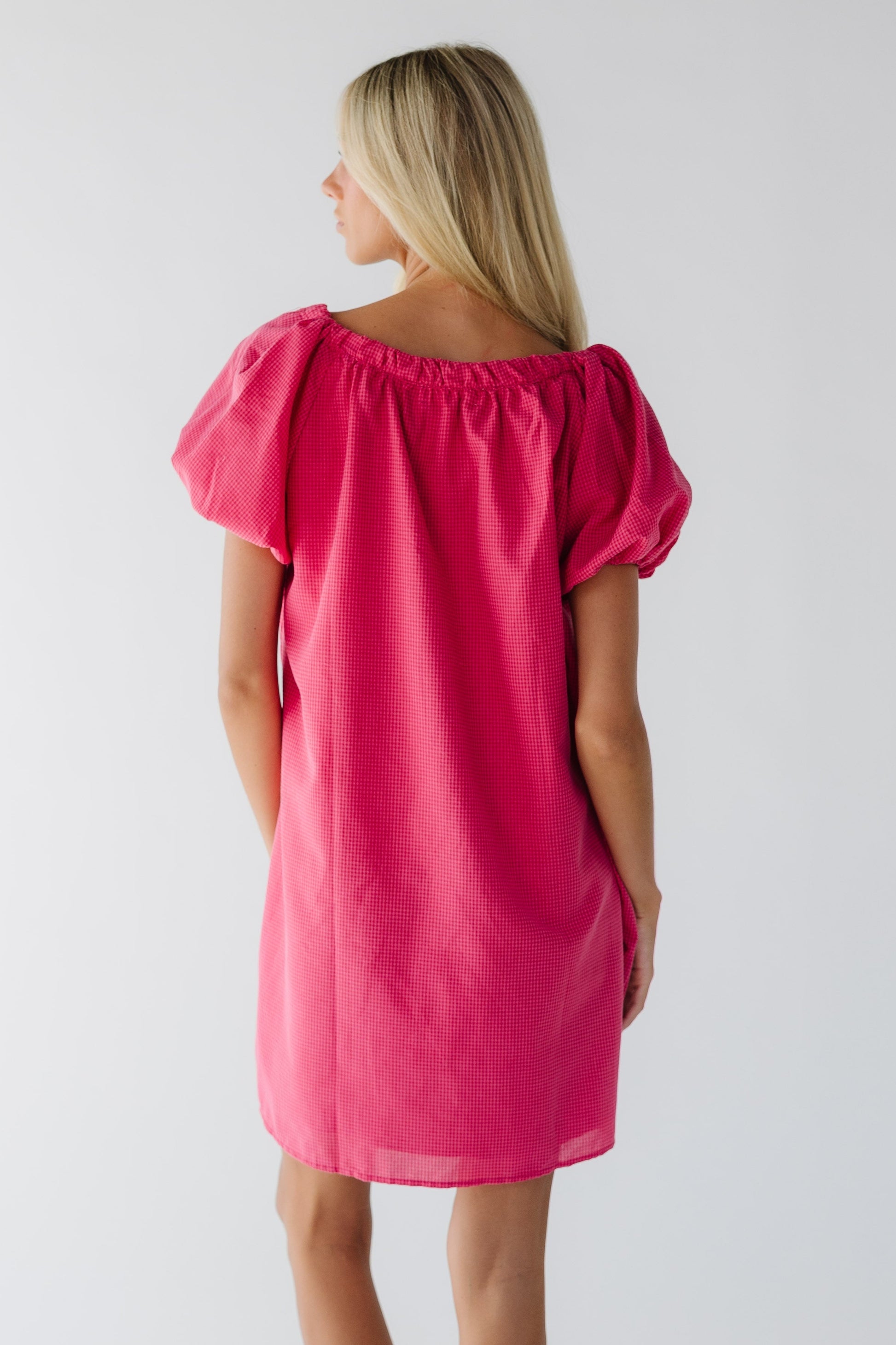 Back view of a woman wearing a pink & red gingham dress with balloon sleeves and a wide scoop neckline.