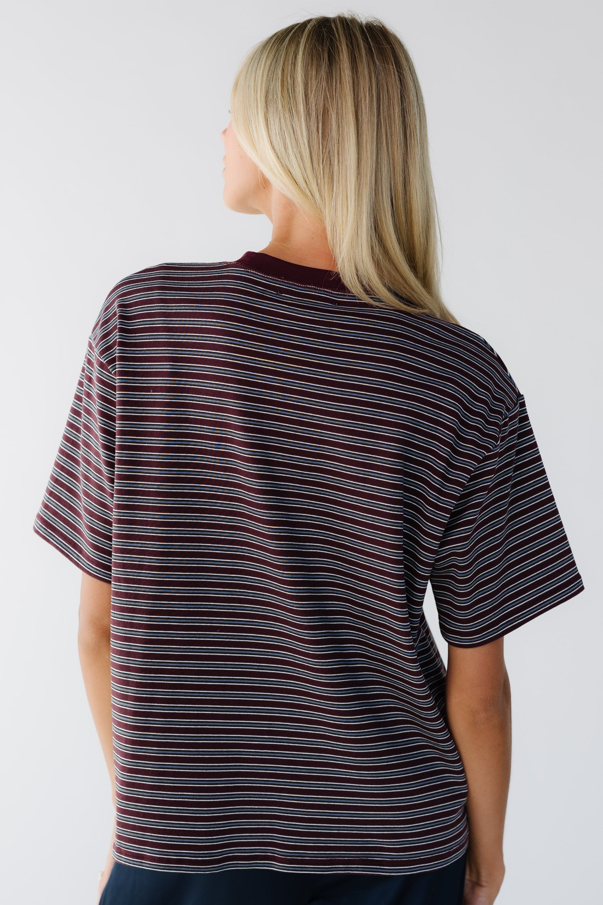 Back view of a woman wearing an oversized short sleeve tee in burgundy and grey stripe.