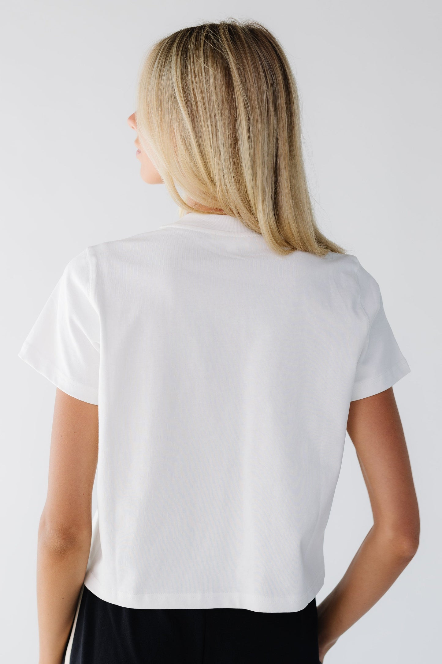 Back view of a young woman wearing a white loose fitting tee with short sleeves.
