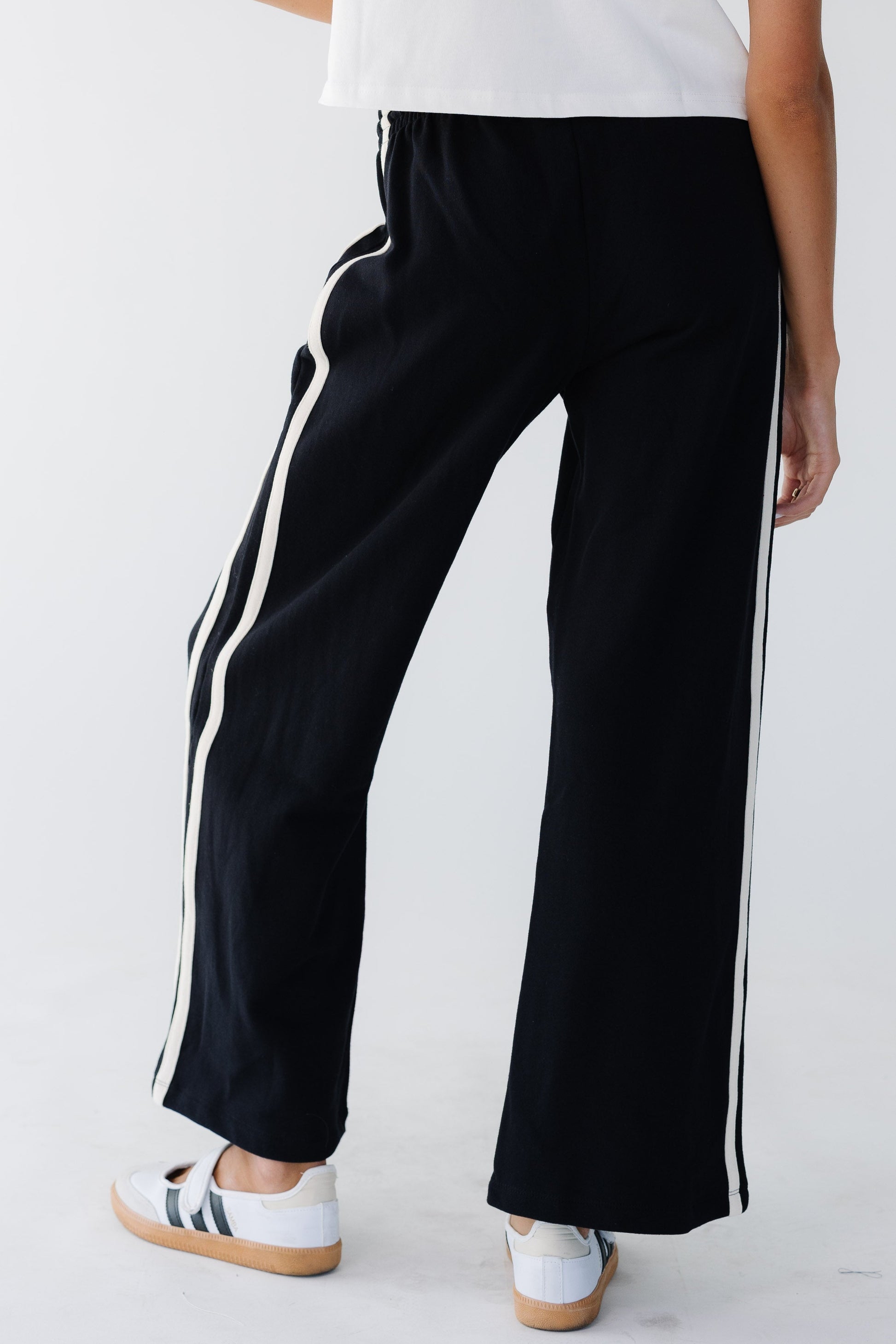 Back view of a young woman wearing wide leg knit athletic pants with 2 white stripes down the sides
