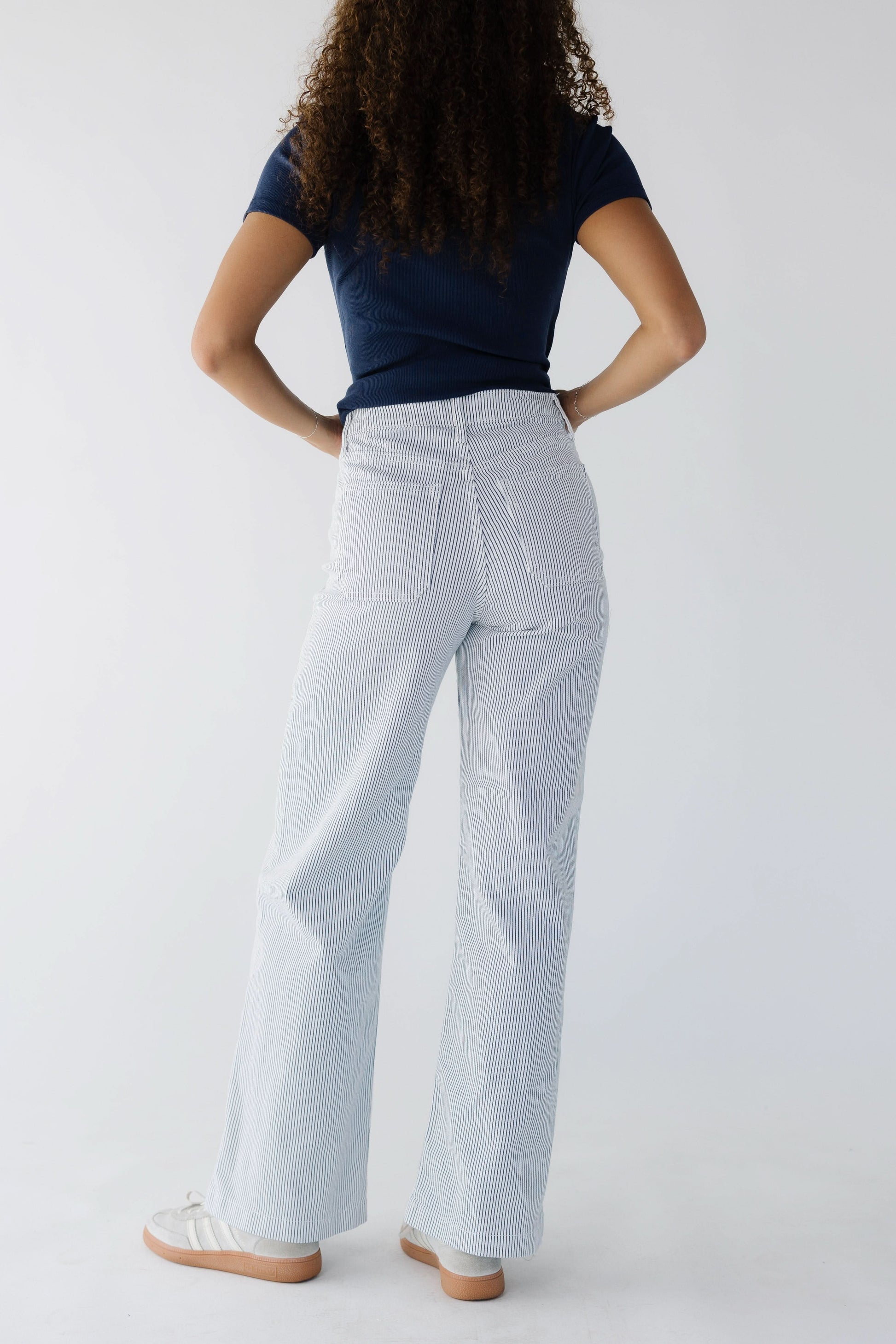 Back viewof a teenage girl wearing a pair of white & navy stripe jeans wtih 2 back patch pockets and a wide cut leg.