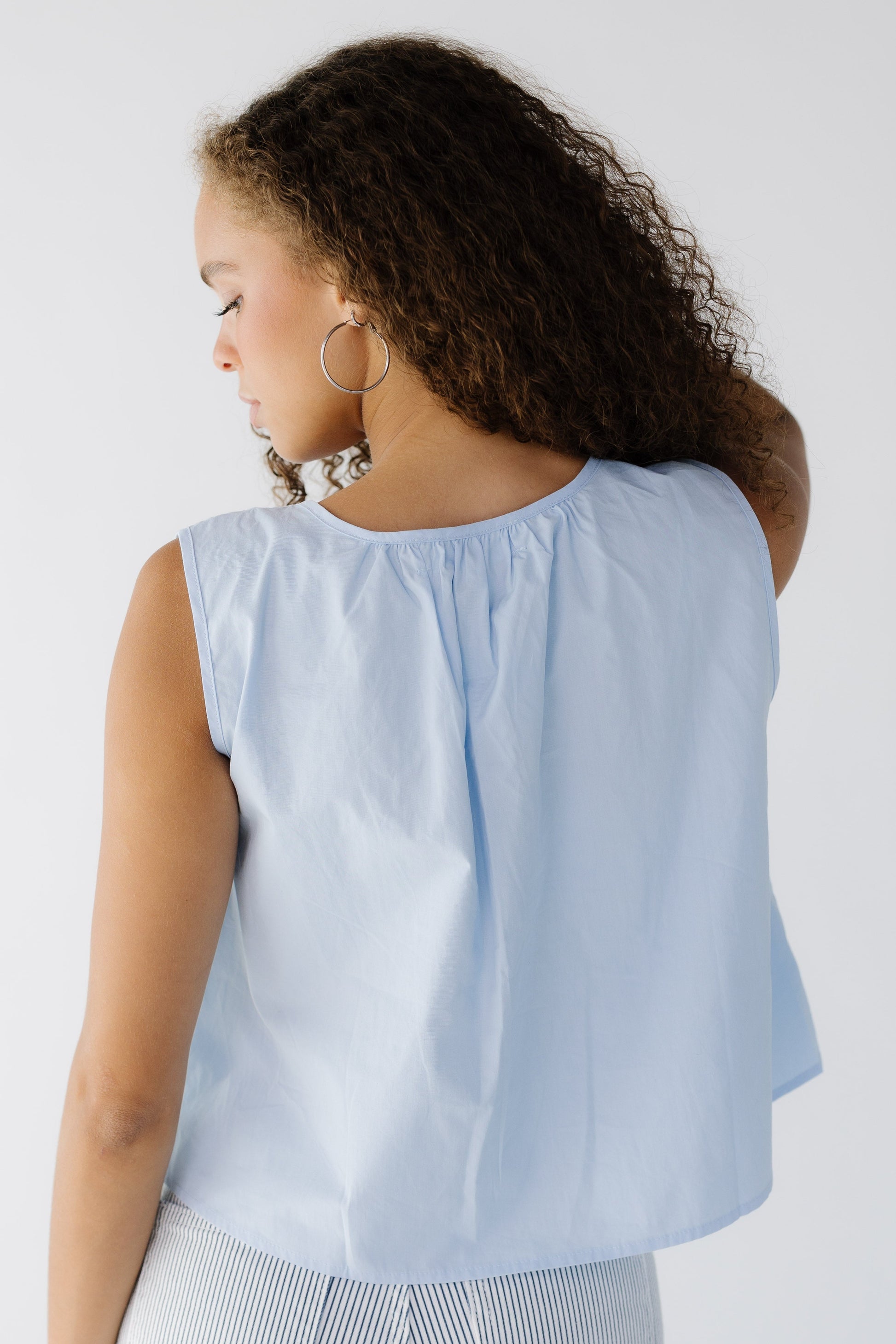 Back view of a woman wearing a loose fitting sleeveless in light blue.