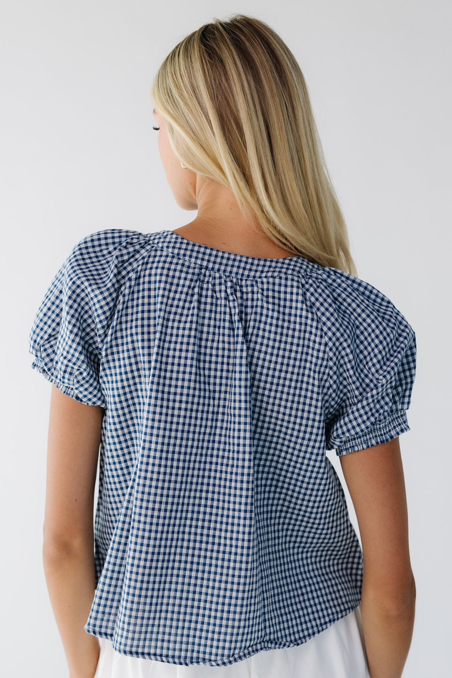 Back view of a woman wearing a loose fitting navy & white gingahm blouse with short puff sleeves