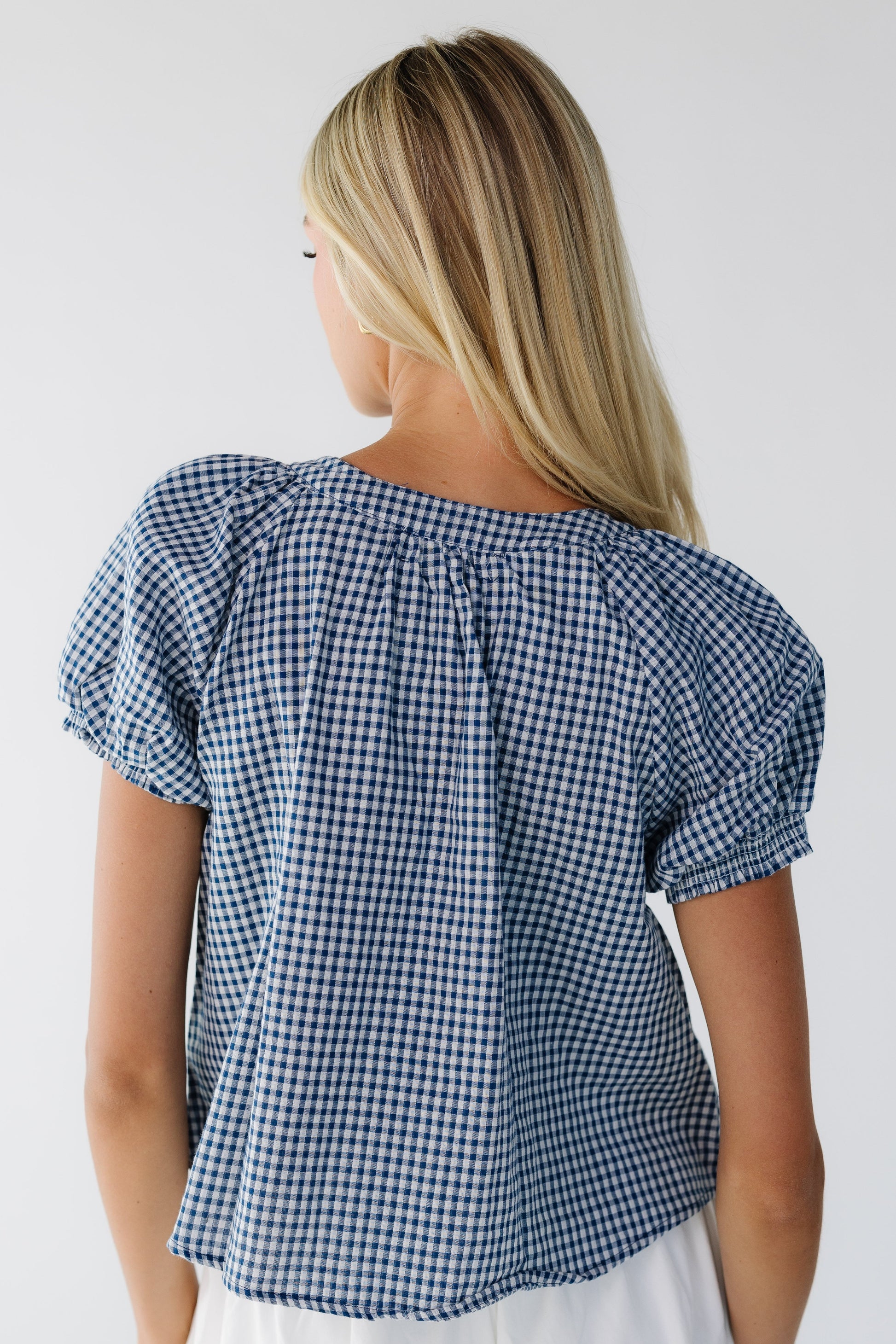 Back view of a woman wearing a loose fitting navy & white gingahm blouse with short puff sleeves