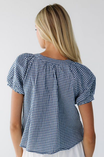 Back view of a woman wearing a loose fitting navy & white gingahm blouse with short puff sleeves