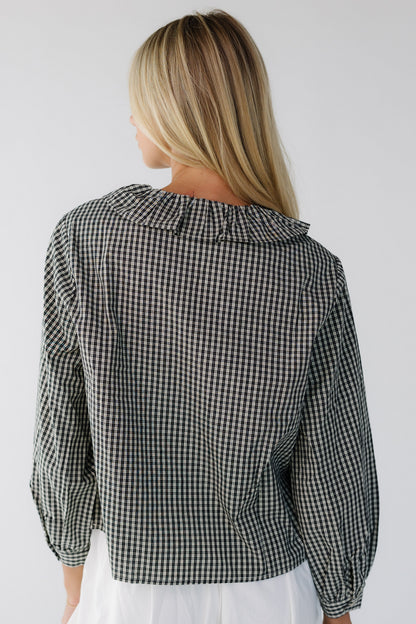 Back view of a woman wearing a black plaid loose fitting blouse with long sleeves and a ruffled collar.
