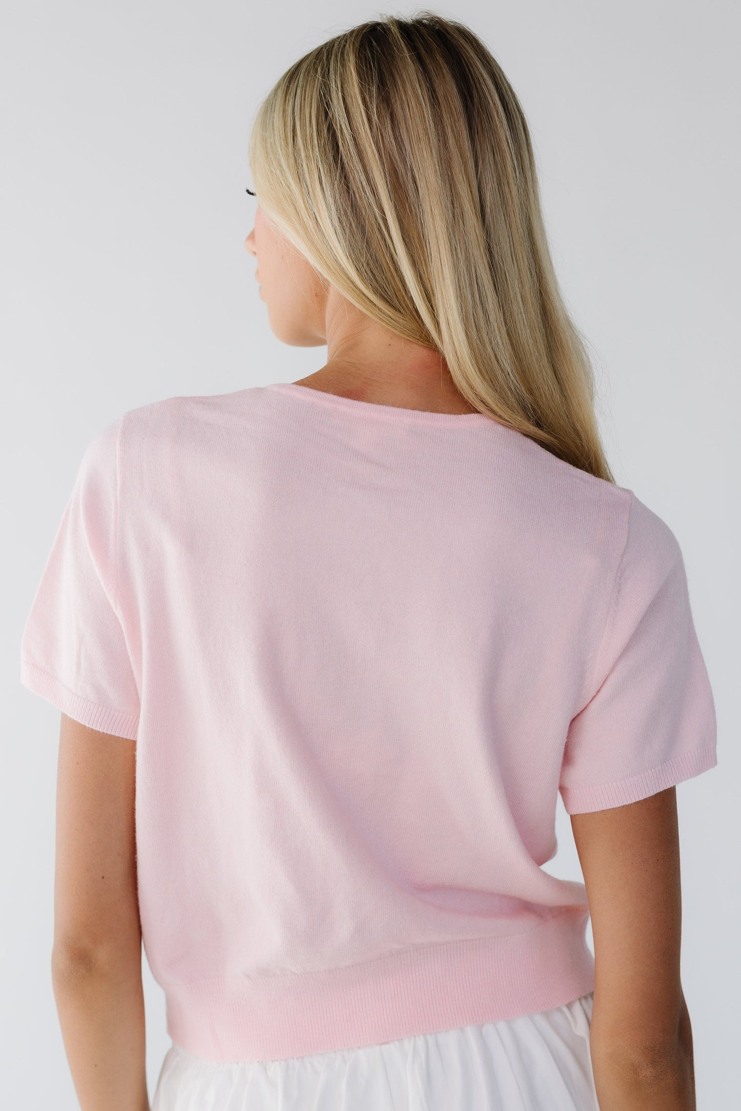Back view of a woman wearing a light pink short sleeve sweater.
