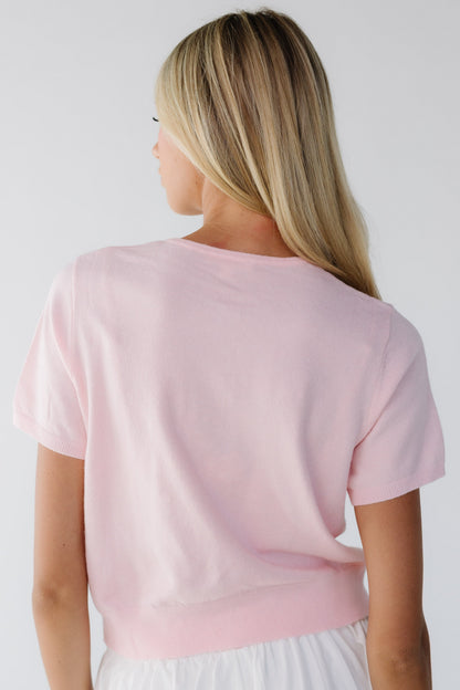 Back view of a woman wearing a light pink short sleeve sweater.