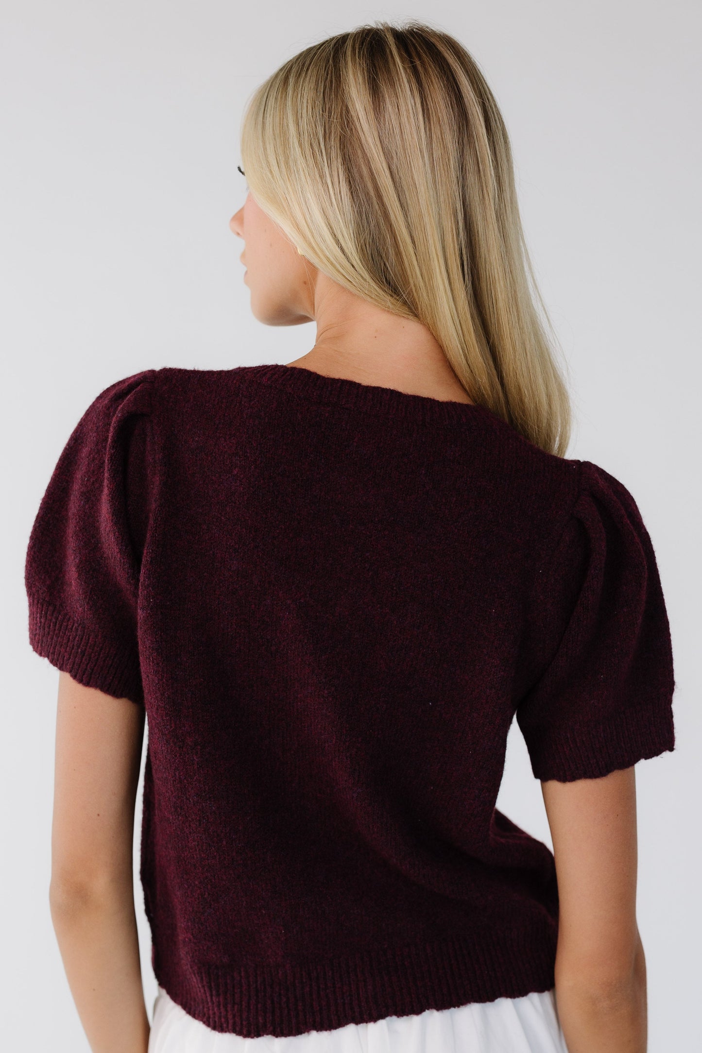 Back view of a young woman wearing a slightly loose fitting cardigan sweater with short sleeves.