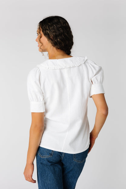 Back view of white woven top with short sleeves and collar with narrow ruffled edge