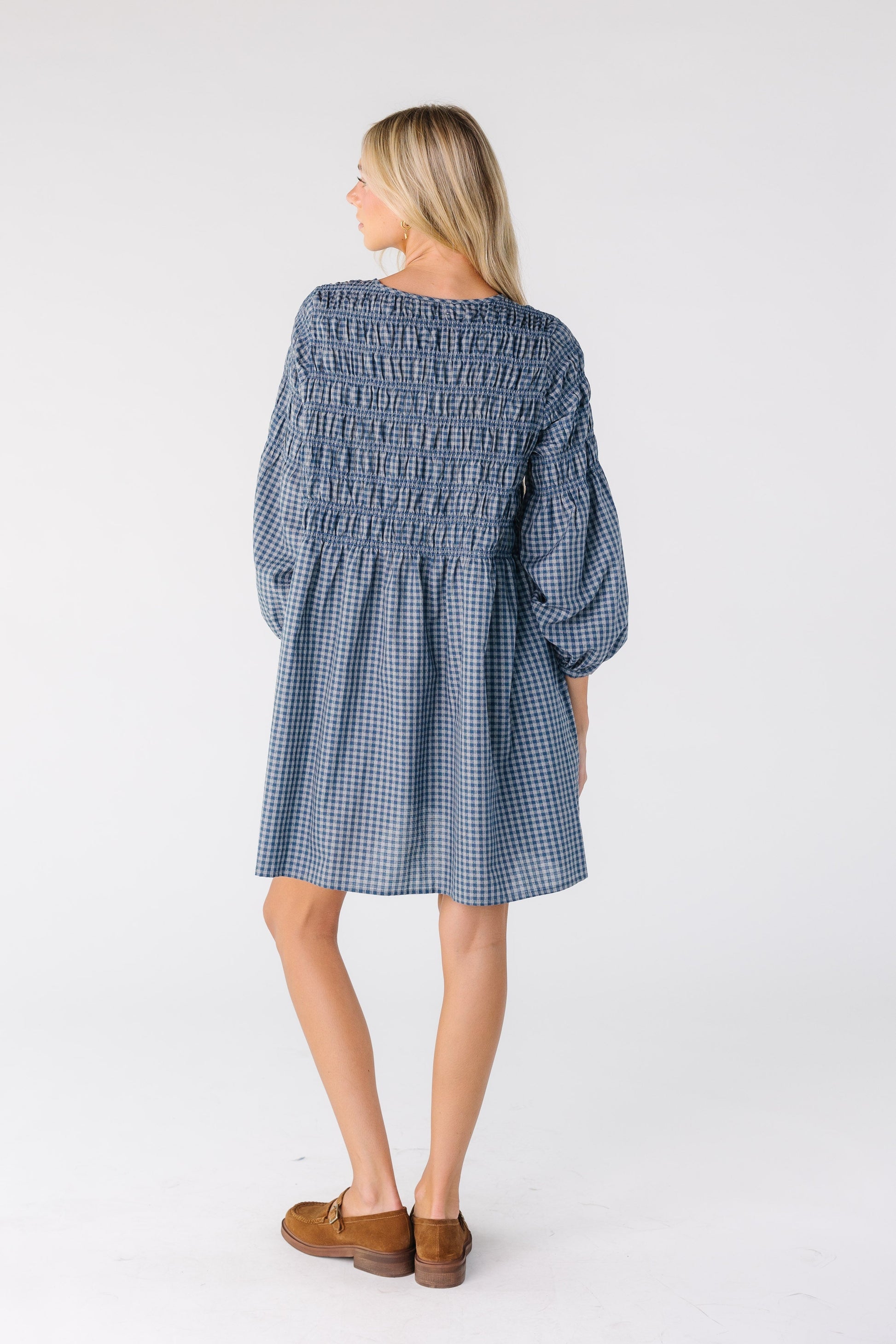 Back view of a woman wearing a loose fitting knee length dress in blue gingham