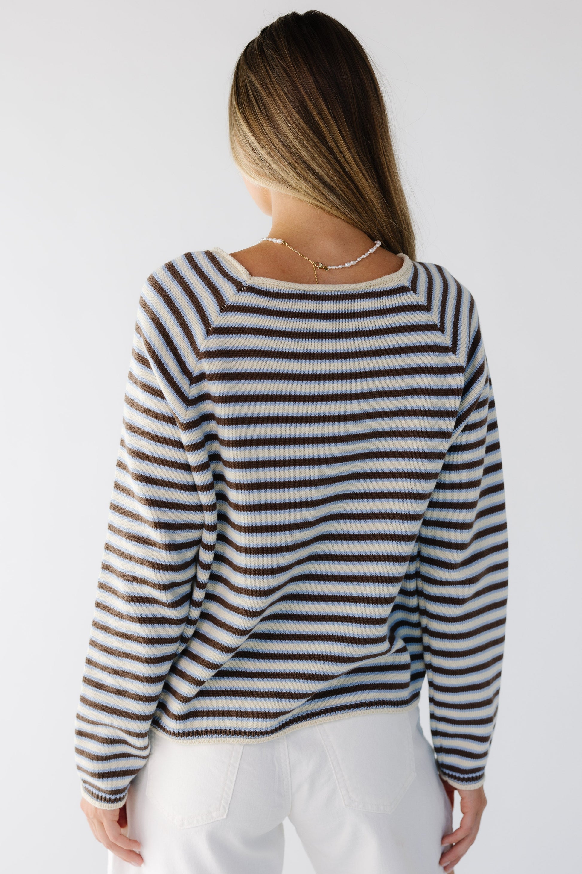Back view of a young woman wearing a cream, brown & blue loose fitting sweater with long sleeves.