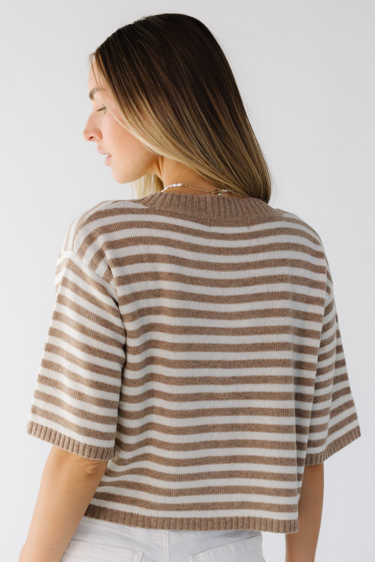 Back view of a woman wearing a cream & taupe stripe cardigan with elbow length sleeves.
