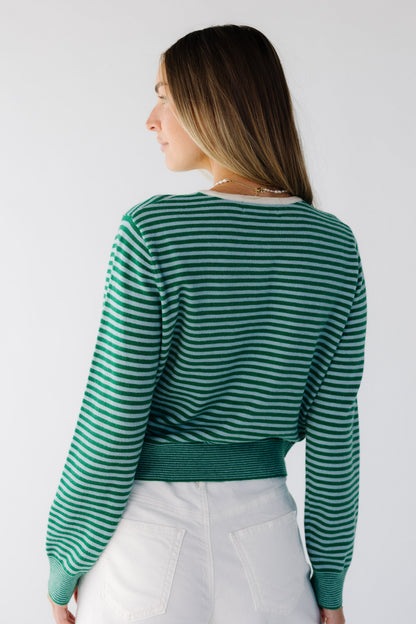 Back view of a young woman wearing a green & light blue stripe cardigan with long sleeves.