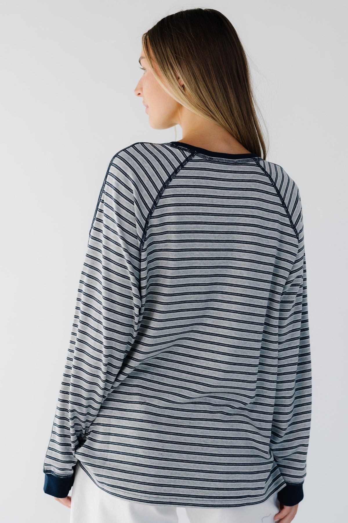 A back view of a woman weairng a grey & navy stripe, loose fitting tee with exposed seams.