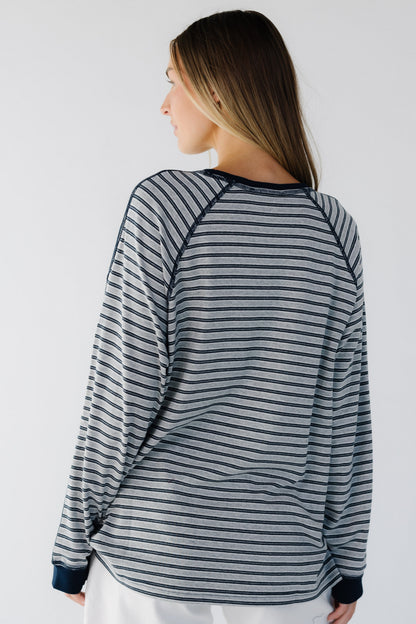 A back view of a woman weairng a grey & navy stripe, loose fitting tee with exposed seams.