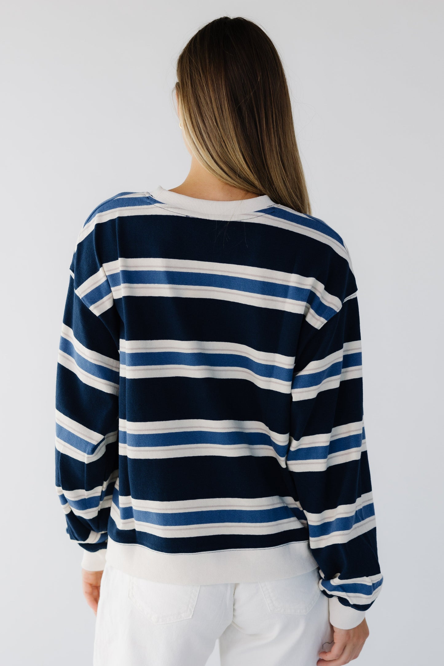 Back view of a woman wearing a loose fitting navy, blue & white stripe sweatshirt with long sleeves.