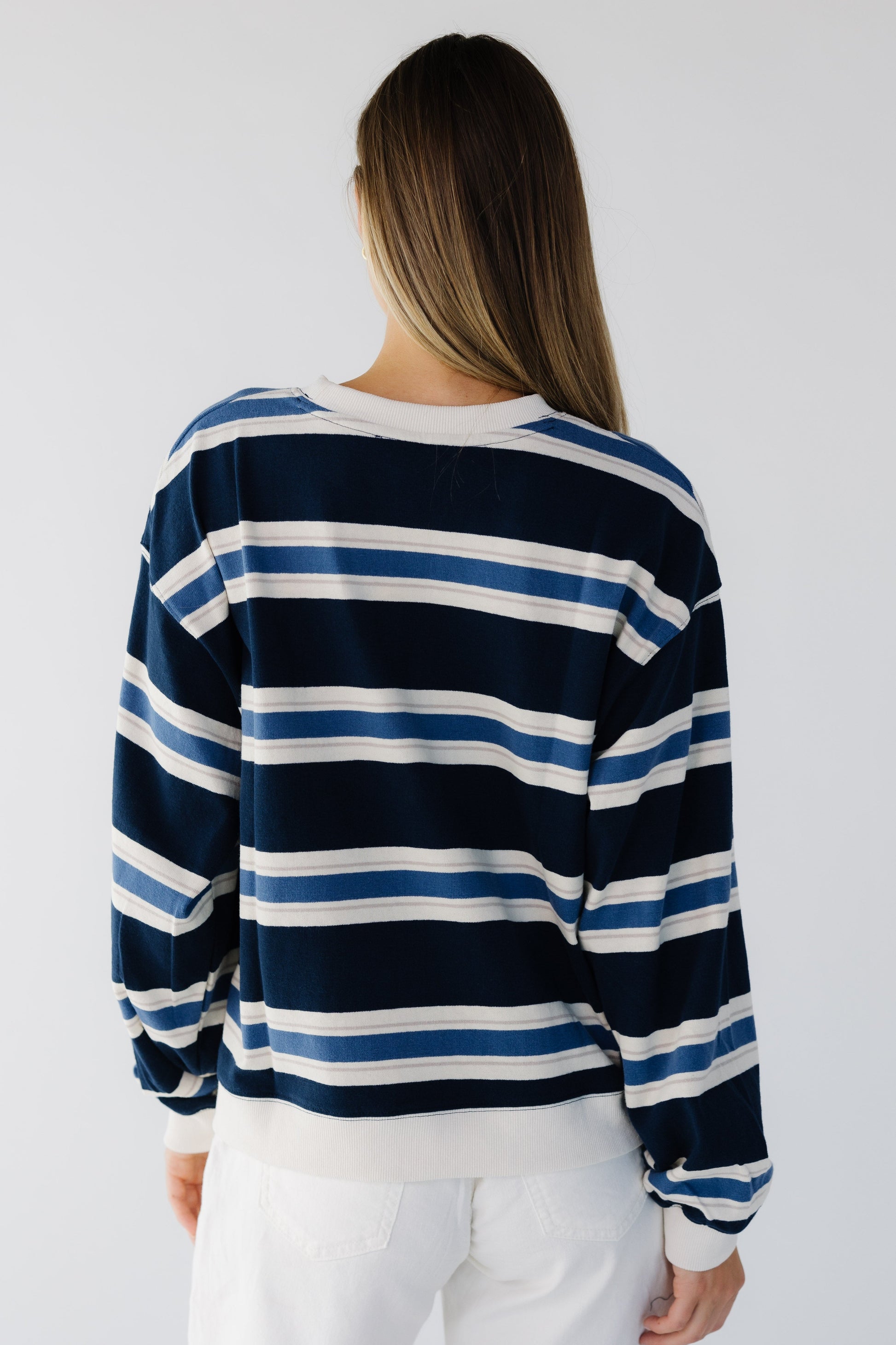 Back view of a woman wearing a loose fitting navy, blue & white stripe sweatshirt with long sleeves.