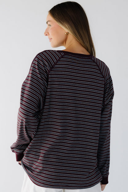 A back view of a woman wearing a burgundy & grey stripe long sleeve tee with exposed seam details.